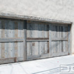 In this photograph, you can appreciate a double-car garage door that is handcrafted out of reclaimed fir lumber. The natural silvers and grays of the wood are vivid and a result of decades of exposure to the elements. This garage door’s design is simple but quite versatile so it can be used in many architectural-style projects. The trim work divides the door into three sections, each with a horizontal trim through the middle. The background of the trim consists of vertical tongue and groove planks that are handpicked for grain and color perfection. Due to its versatility, this custom reclaimed wood garage door can be applied to old-world European-style homes!